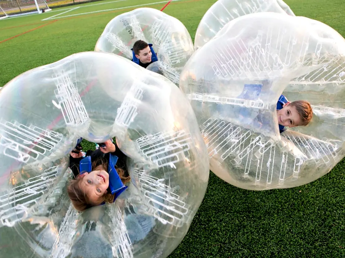 Kids lying on grass inside large transparent bubbles after a bubble soccer game