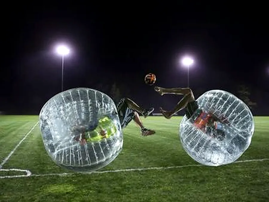 Two people playing bubble soccer at night under stadium floodlights